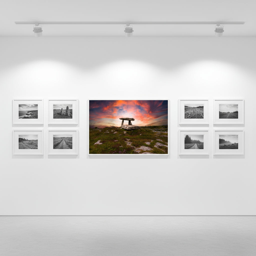 Dolmen print as the focal art piece on gallery-white walls, matte oak frame, spotlights overhead, alongside smaller black-and-white landscape prints.
