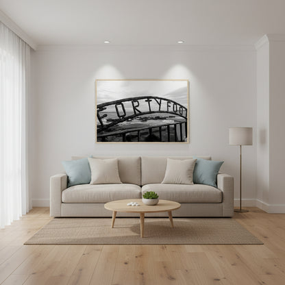 Modern coastal living room with white walls, oak floors and linen sofa; natural wood frame; Forty Foot photograph as focal point under discreet gallery spotlights.
