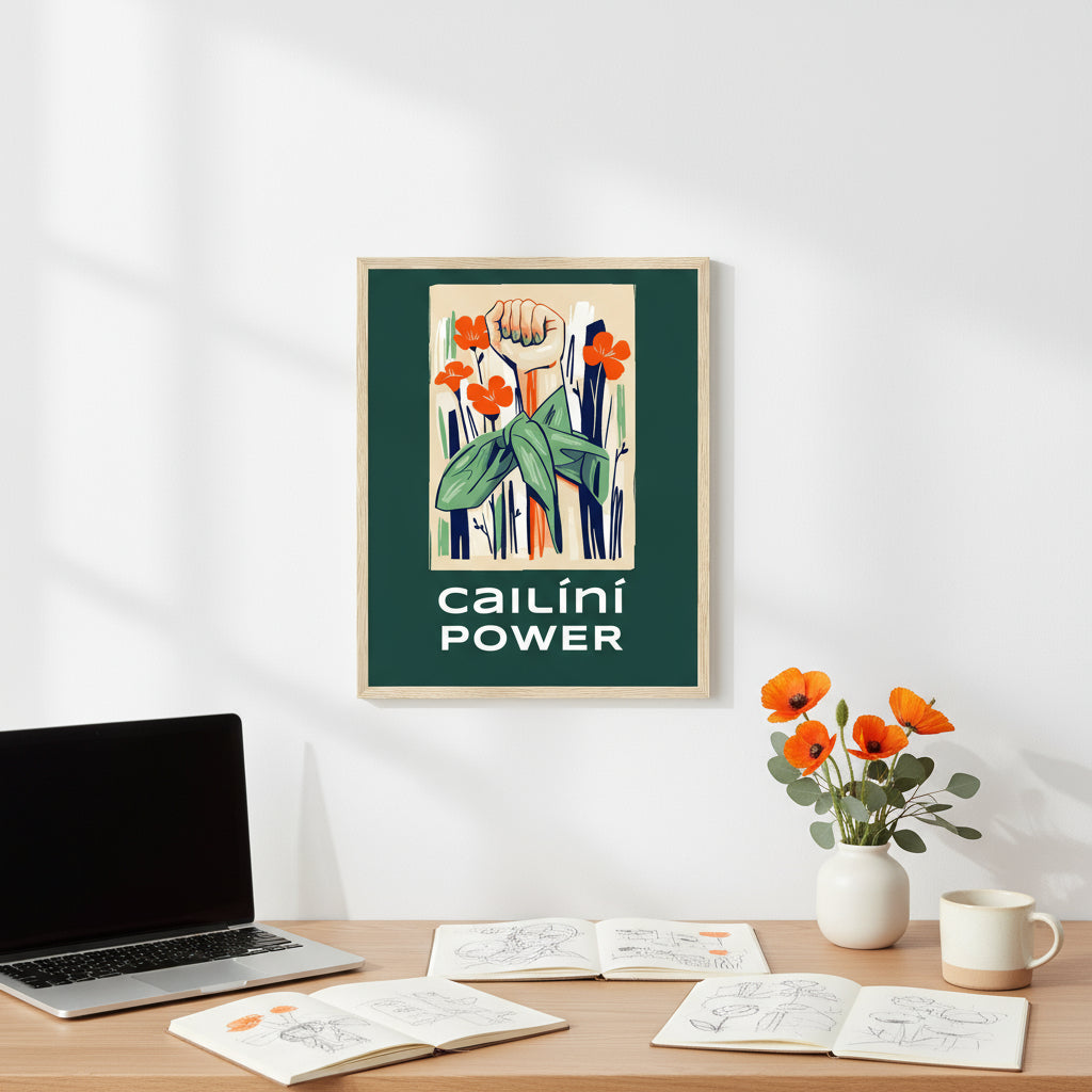 Framed “Cailíní Power” print on a white studio wall above an oak desk with sketchbooks, MacBook, fresh flowers and ceramic mug — minimalist, airy, empowering.”