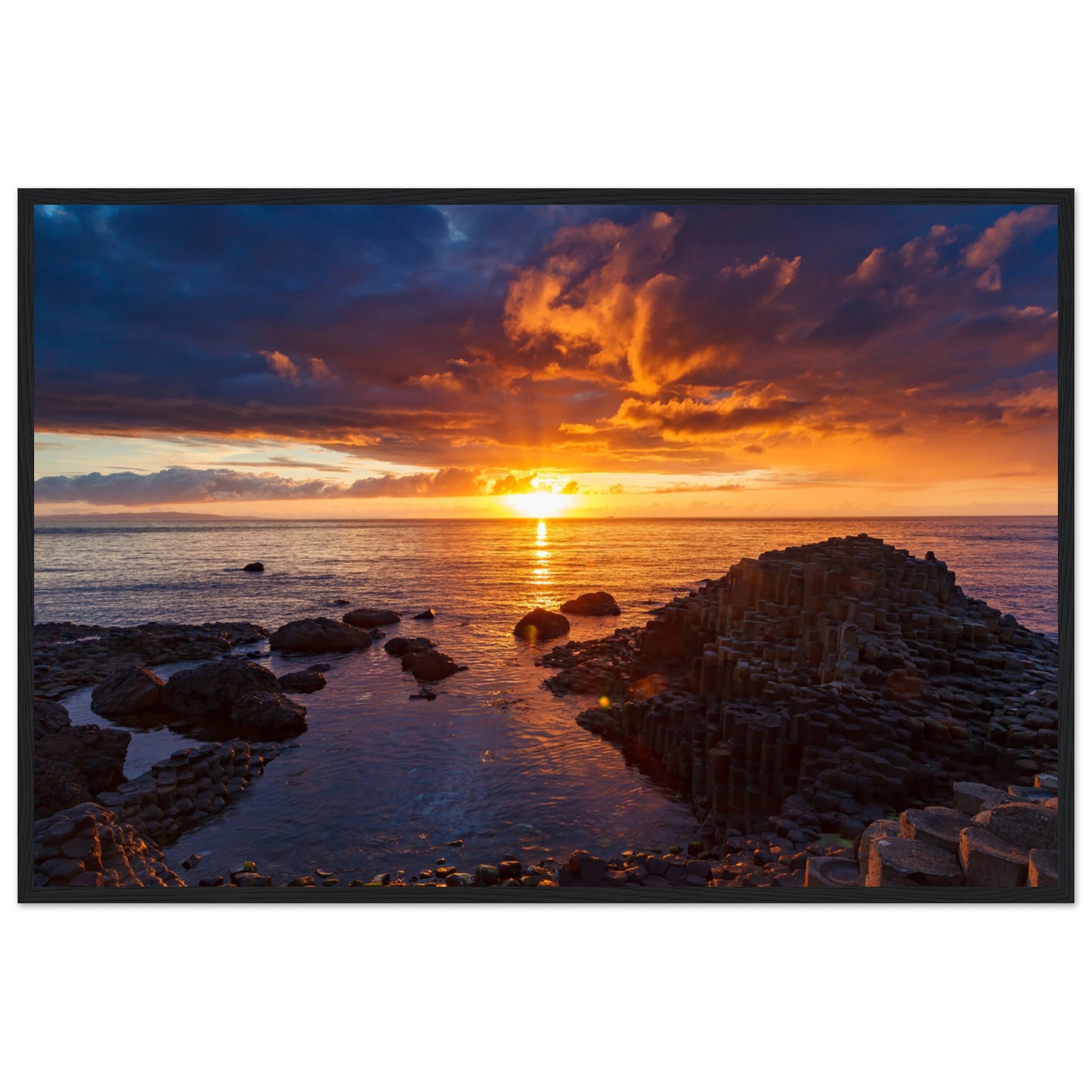 Framed art print of a mesmerizing sunset at Giant's Causeway, showcasing iconic basalt columns against a sky painted with warm hues. The scene captures nature's beauty and tranquility, adding a sophisticated touch to home or office decor. Perfect for any art lover.